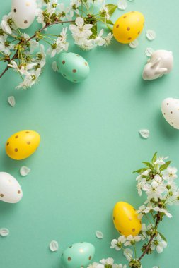 Pastel dikey Paskalya yumurtaları sarı, nane ve yeşil bir zeminde beyaz çiçeklerin arasında dinleniyor, parlak bir bahar havası yakalıyor ve tebrik kartları ve mevsimlik dekorlar için mükemmel bir Paskalya kutlaması.