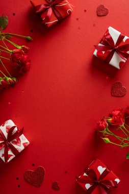 Hediye kutuları, güller ve kalp aksanlarıyla dolu canlı dikey kırmızı arka plan, sıcak bir sevgililer günü havası yaratır. Aşkı, hediyeyi ve içten selamları kutlar.