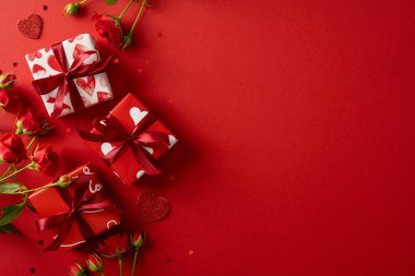 Kırmızı hediye kutuları, kalpler ve güllerin cesur kırmızı bir zemine karşı sergilendiği romantik bir sahne. Sevgililer Günü terfileri, selamlar ve kart tasarımları için mükemmel.