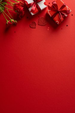 Kırmızı arka planlı, hediyeli, kurdeleli ve kalp aksanlı romantik bir sevgililer günü sahnesi. Aşk, hediye ve kutlama için mükemmel sıcak bir ortam.