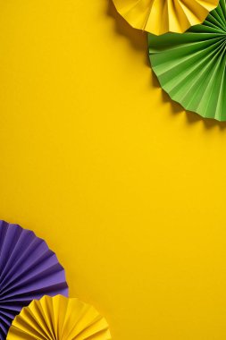 Mor ve yeşil kağıt yelpazeli, dikey sarı arka plan Mardi Gras kutlamaları, davetiyeler, afişler ve yaratıcı kampanyalar için uygun bir şenlik havası yaratıyor.