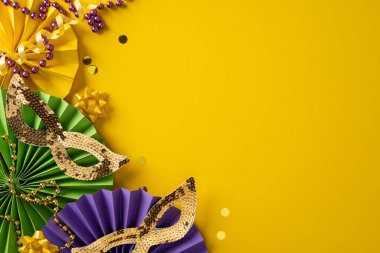 Canlı Mardi Gras sahnesinde sarı bir zemin üzerinde pullu maskeler, kağıt yelpazeler, boncuklar ve konfetiler vardı. Şenlik havası, karnaval tarzı, renkli dokular, kutlama havası, parti aksesuarları.