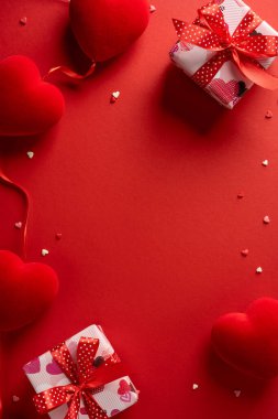 Kırmızı kalplerin olduğu dikey bir sevgililer günü sahnesi, kırmızı kurdeleli hediye kutuları, ve canlı kırmızı bir arkaplanda dağınık küçük süslemeler. Romantik kutlama, aşk ve hediye teması için ideal.