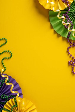 Sarı arka plan, mor ve yeşil boncuk çelenkler ve dekoratif hayranlarla dolu canlı Mardi Gras sahnesi bir karnaval kutlaması için şenlikli bir davet havası yaratıyor.