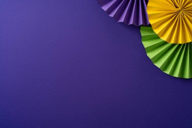 Morumsu arka planda canlı bir karnaval sahnesi ve sarı yeşil ve mor renkli rosetler Mardi Gras bayramını ve parti havasını temsil ediyor.