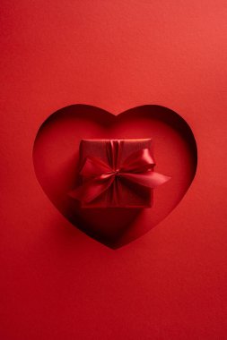 Canlı, dikey, kırmızı arka plan, kalp şeklinde bir kesit. Saten bir kurdeleyle sarılmış bir hediyeyi gözler önüne seriyor. Romantizm, aşk ve sevgililer gününü cesur sinematik bir sunumla yakalıyor.