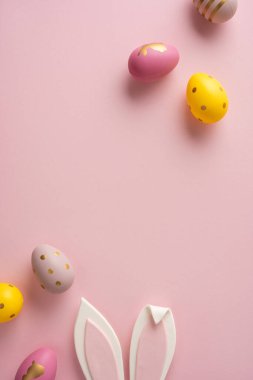 Pastel dikey yumurtalar ve pembe arka planda tavşan kulakları sıcak bir Paskalya havasını çağrıştırıyor tebrik kartları, mevsimsel içerik ve bahar kutlamaları için mükemmel.