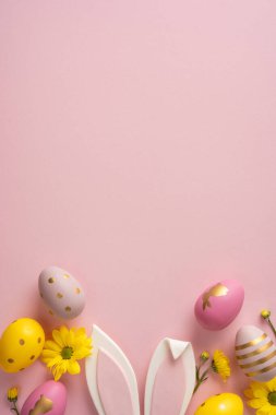 Yumuşak dikey pembe arkaplan vitrinleri pastel yumurtalar, beyaz tavşan kulakları ve parlak çiçekler, tebrik kartları, mevsimsel promosyonlar ve festival ürünleri tasvirleri için ideal bir Paskalya sahnesi yaratıyor.