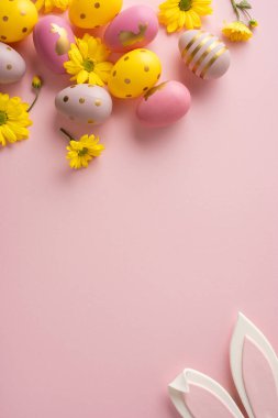 Pastel dikey altın noktalı ve çizgili yumurtalar yumuşak pembe bir zeminde parlak sarı çiçeklerin arasında oturur. Kutlama kartları ve bahar promosyonları için mükemmel bir Paskalya sahnesi yaratır.