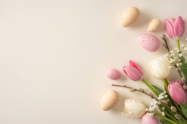Paskalya yumurtaları ve laleler yumuşak bej bir zeminde dinleniyor. Bahar kutlamaları ve Paskalya kutlamaları için mükemmel bir ortam yaratıyor.