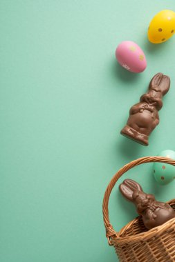 Mutlu Paskalya kutlamaları. Çikolata tavşanı ve pastel yeşil bir arka planda hasır sepete boyanmış yumurta. Bahar kutlaması ve tatlı mevsimlik ikramlar.