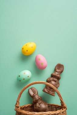 Mutlu Paskalya kutlamaları. Çikolata tavşanları ve hasır sepette süslenmiş yumurtalar mevsimlik kutlama ve şenlikli dekorasyon için yumuşak yeşil bir arka planda.