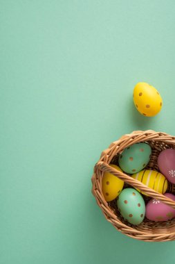 Hasır bir sepette boyalı pastel yumurtaların olduğu mutlu Paskalya dikey selamlaşmaları. Nane arkaplanında neşeli bahar kutlamaları ve neşeli mevsimlik dekorasyonlar.