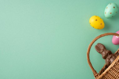 Hasır bir sepete yerleştirilmiş, yumuşak pastel arka planda yumurtaları olan çikolatalı bir tavşanın bayram kartları ve mevsimlik promosyonlar için ideal olduğu Paskalya kutlamaları sahneniz kutlu olsun.