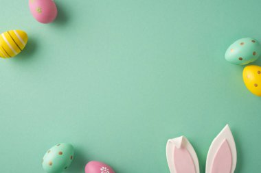 Mutlu Paskalya kutlamaları. Pastel süslemeli yumurtalar ve nane yeşili arka planda neşeli tavşan kulakları mevsimlik kartlar, davetiyeler, bahar promosyonları ve tatil tasarımları için ideal.