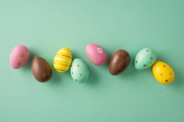 Renkli dekorasyon ve nane yeşili arka planda çikolata yumurtalarının yer aldığı Paskalya bayramınız kutlu olsun. Bahar kutlaması ve mevsimlik dekorasyon için.