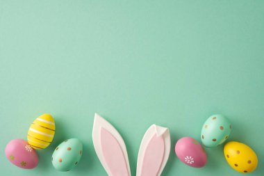 Mutlu Paskalya kutlamaları ve tavşan kulaklı ve pastel boyalı yumurtalar. Nane yeşili bir arka planda düzenlenmiş bahar tatili sahnesi için.