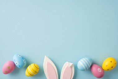 Bahar kutlaması ve tatil kartı tasarımı için yumuşak mavi arka planda pastel süslemeli yumurtalar ve neşeli tavşan kulaklarının yer aldığı Paskalya kutlamanız kutlu olsun.