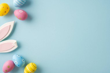 Pastel süslemeli yumurta ve neşeli tavşan kulaklarının yer aldığı Paskalya kutlamalarınız kutlu olsun. Bahar kutlaması ve mevsimlik dekorasyon için yumuşak mavi bir arka planda düzenlenmiştir.