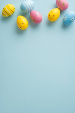 Pastel boyalı yumurtalarla, bahar kutlaması için yumuşak mavi arka plan boyunca düzenlenmiş Paskalya bayramın kutlu olsun.