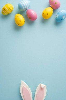 Pastel dikey dekore edilmiş Paskalya yumurtaları ve yumuşak mavi arka planda tavşan kulakları mutlu bir Paskalya kutlaması ve selamlama iletiyor.