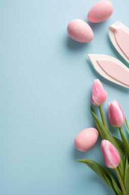 Pembe benekli yumurtalar, hassas laleler ve pastel mavisi arka planda düzenlenmiş dekoratif tavşan kulakları içeren Paskalya bayramın kutlu olsun.