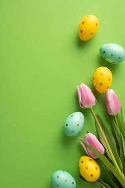 Parlak dikey mutlu paskalyalar pastel puantiyeli yumurtalar ve yeşil arka planda dizilmiş pembe laleler.