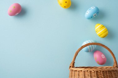 Hasır sepetten dökülen pastel yumurtaların mevsimlik kutlama kartları posterleri ve bahar tatili tasarımları için mükemmel yumuşak mavi bir zemin üzerine yerleştirildiği Paskalya kutlamanız kutlu olsun.