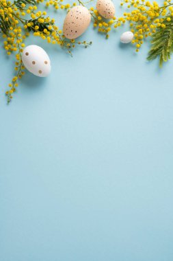 Süslü yumurta ve parlak sarı mimoza çiçeğinin yer aldığı mutlu Paskalya dikey düzlükleri mavi arka planda tatil tebrik kartı, bahar tanıtımı ve mevsimsel tasarım projesi için idealdir.