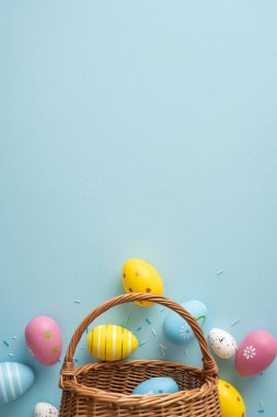 Mutlu Paskalya Bayramı boyalı pastel yumurta ve hasır sepetten dökülen konfetileri neşeli bahar kutlamalarını anlatan mavi bir arka planda.