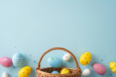 Hasır sepetten dökülen boyalı yumurtalarla dolu neşeli Paskalya sahnesi yumuşak pastel arka planda, bahar şenlik dekorasyonunu ve neşeli kutlamaları aktarıyor.