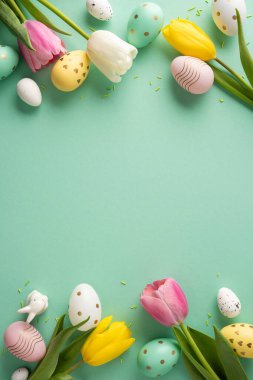 Renkli pastel yumurtaların ve lale çiçeklerinin nane arkaplanındaki Paskalya dikey düzenlemesi ilkbahar kutlamalarını ve parlak mevsimsel havayı çağrıştırıyor.