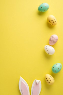 Pastel boyalı yumurta ve tavşan kulaklı, bahar dekorasyonu için parlak sarı bir arka planda ve bayram minimumu düz bir zeminde Paskalya bayramınız kutlu olsun.