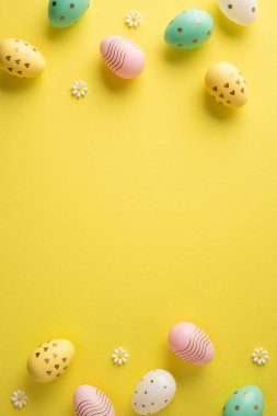 Parlak dikey pastel Paskalya yumurtaları ve küçük papatya çiçekleri canlı sarı bir arkaplanda mevsimsel kutlamalar için bahar sıcağı ve şenlikli bir dekorasyon sunuyor.