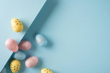 Mutlu Paskalya pastel yumurtaları altın kalpli ve dalga aksanlı yumuşak mavi bir yüzeye dizilmiş. Minimum bir bahar kompozisyonu yaratıyor.