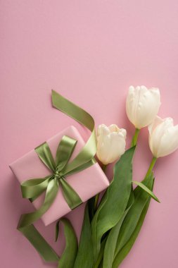 Pink wrapped present with green satin ribbon paired with white tulips on a soft pastel background conveying Mother's Day love and elegant spring celebration