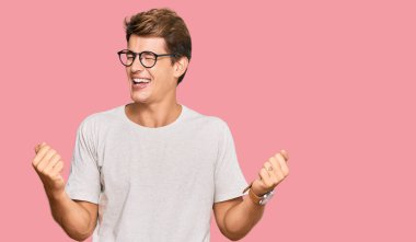 Yakışıklı beyaz adam, günlük kıyafetler ve gözlük takıyor. Çok mutlu ve heyecanlı. Kolları havada, gülümsüyor ve başarı için bağırıyor. kutlama konsepti. 