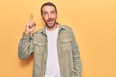 Gündelik giysiler giymiş genç yakışıklı bir adam başarılı bir fikri işaret ediyor. Heyecanlı ve mutlu. Bir numara.. 