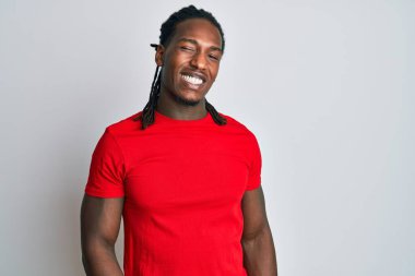 Saçları günlük kıyafetlerle örülmüş, kameraya seksi bir ifadeyle bakan, neşeli ve mutlu yüzlü Afro-Amerikan bir adam.. 