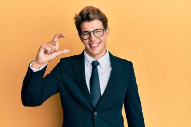 İş elbisesi giyen, kravat takan, gülümseyen, kendine güvenen, el hareketi yapan, parmaklarıyla işaret yapan yakışıklı beyaz bir adam ve kamera. ölçüm kavramı. 