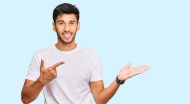 Gündelik beyaz tişört giyen genç yakışıklı adam kameraya hayret ediyor ve gülümsüyor.. 