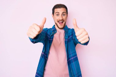 Gündelik giysiler giyen genç bir adam elinle olumlu jest yapıyor, gülümsüyor ve başarı için seviniyor. kazanan jest. 