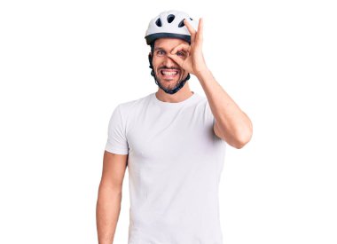 Bisiklet kaskı takan yakışıklı genç adam el hareketleriyle gülümsüyor, gözleriyle mutlu yüzüyle parmaklarının arasından bakıyor.. 