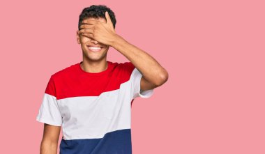 Genç, yakışıklı, Afro-Amerikalı sıradan kıyafetler giyen, gülümseyen ve gülümseyen bir adam. Gözleri şaşkınlıkla örtüyor. kör kavram. 