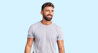 Gündelik kıyafetler giyen genç İspanyol bir adam yüzünde gülümsemeyle yan yana bakıyor, doğal bir ifade. Kendinden emin gülen. 