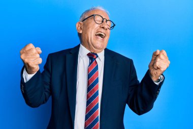 İş elbisesi giymiş, kravatlı, beyaz bir adam kolları havada, gülümseyen ve başarı için bağıran, çok mutlu ve heyecanlı bir jest yapıyor. kutlama konsepti. 