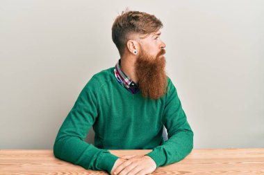 Genç İrlandalı kızıl saçlı adam masaya oturmuş yan yan yan bakıyor, rahat poz veriyor, kendine güvenen bir gülümsemesi var.. 