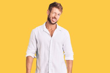 Gündelik giysiler giymiş genç beyaz adam kameraya seksi bir ifadeyle bakıyor, neşeli ve mutlu bir yüzle.. 