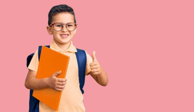 Okul çantası takan, gülümseyen, pozitif gülümseyen ve onaylayan küçük şirin bir çocuk. 