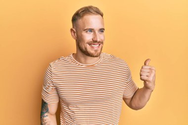 Sıradan çizgili tişört giyen genç beyaz bir adam baş parmağını yana kaldırmış, ağzı açık gülümsüyor. 